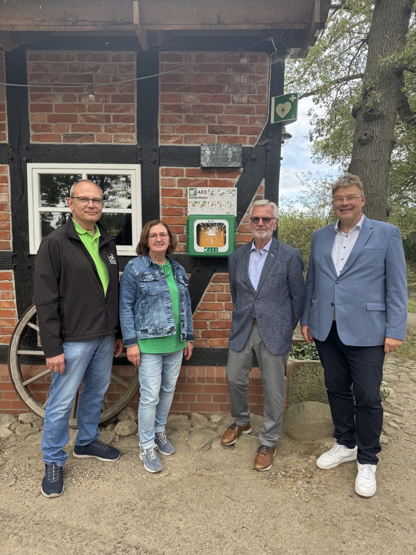 Vier Personen vor einem Fachwerkhaus neben dem neuen Defibrillator-Kasten