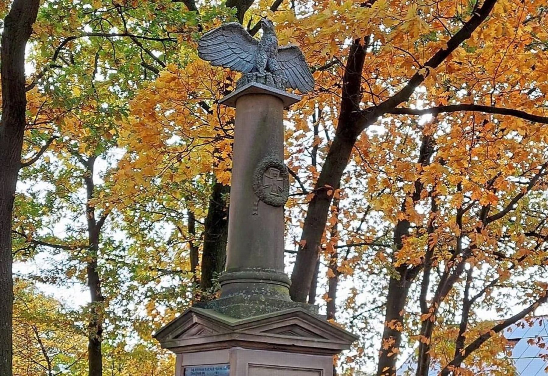 Ehrenmal in Kleinendorf mit Adler auf der Säule, dahinter Herbstlaub